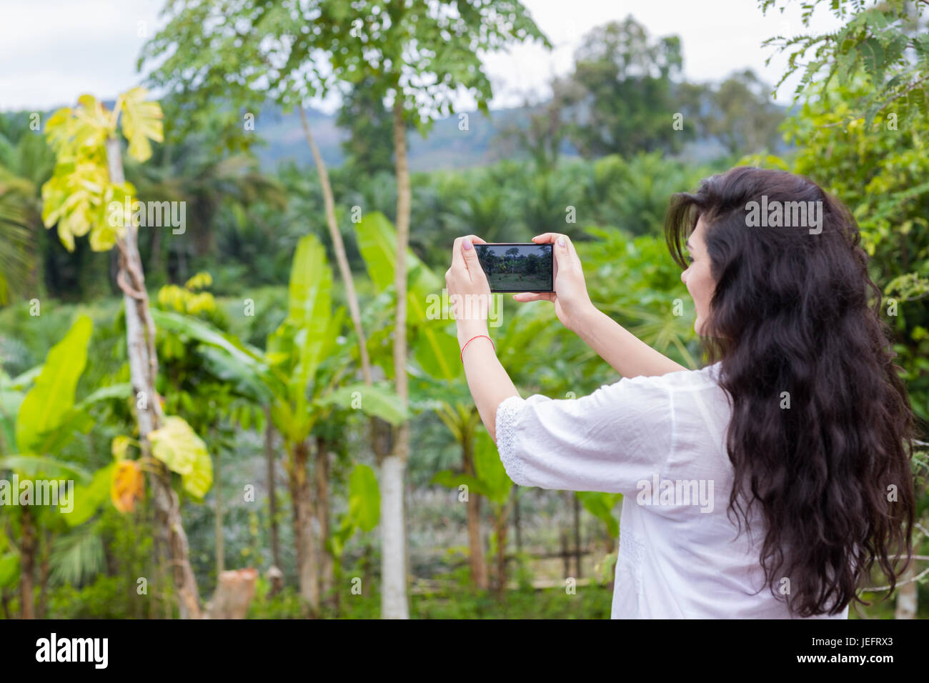 Frau, die Aufnahme der tropische Waldlandschaft auf Handy Smartphone zurück Rückansicht Stockfoto