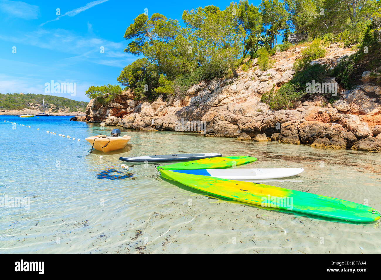 Gelbe Boot und Surfbretter auf idyllischen Cala Portinatx Strand und Klippen Felsen mit Pinien im Hintergrund die Insel Ibiza, Spanien Stockfoto