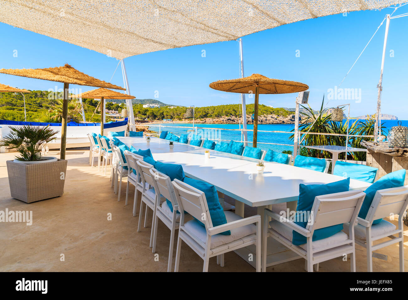 Strand von CALA NOVA, Insel IBIZA - 20. Mai 2017: Weißen Tisch und Stühle mit blauen Kissen auf Restaurant-Terrasse am Strand von Cala Nova mit schönen Blick aufs Meer vie Stockfoto