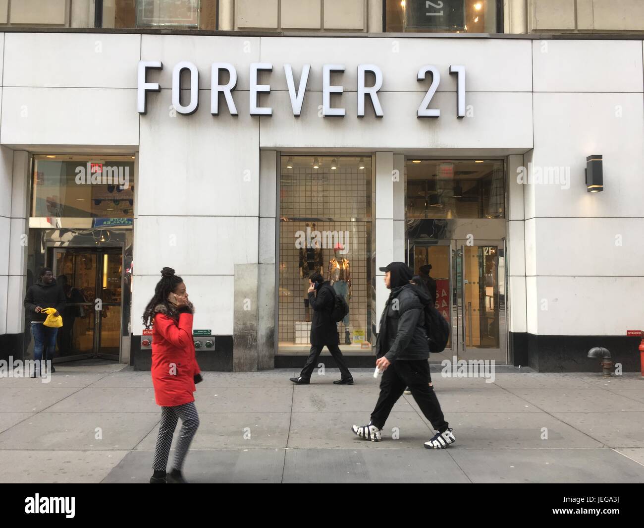 NEW YORK CITY - 1. FEBRUAR 2017: Afroamerikanische Frau in einer roten Jacke hält Mobiltelefon zu Ohr, als sie an der Forever 21-Schaufenster vorbeigeht. Stockfoto