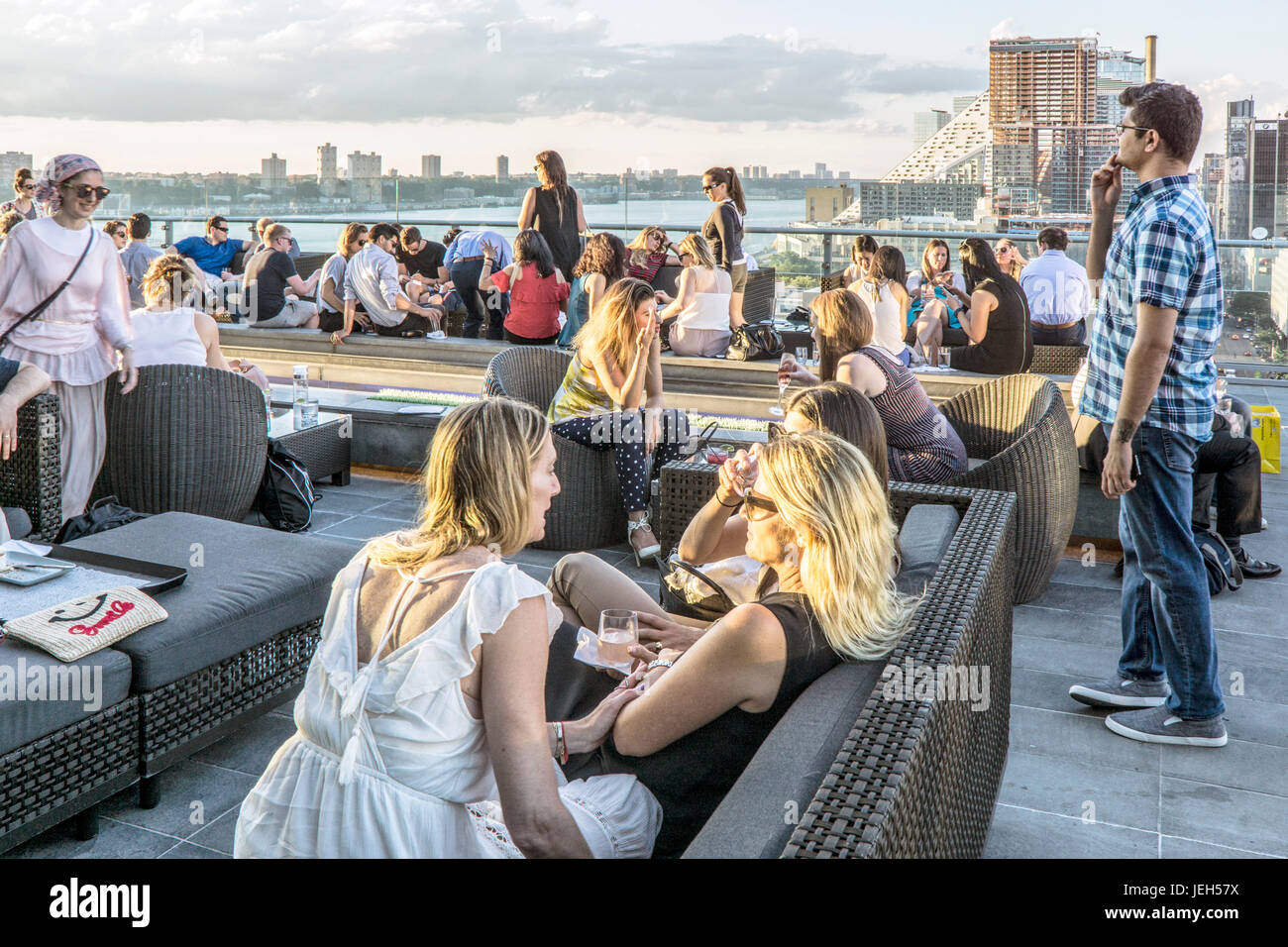 Blick nach Norden über Ink48 Hotel bar Presse-Lounge bei Sonnenuntergang auf dem Dach mit Jugendlichen Geselligkeit im Chat & Blick auf Blick auf Hudson River, untergehende Sonne Stockfoto