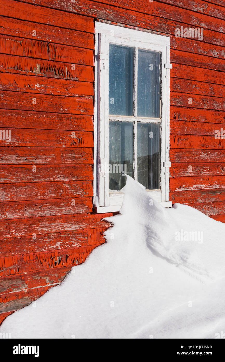 Eine Schneeverwehung berühren das Fenster in einem Gebäude mit einer rot lackierte Holzfassade, die getragen und verwittert ist; Orion, Alberta, Kanada Stockfoto