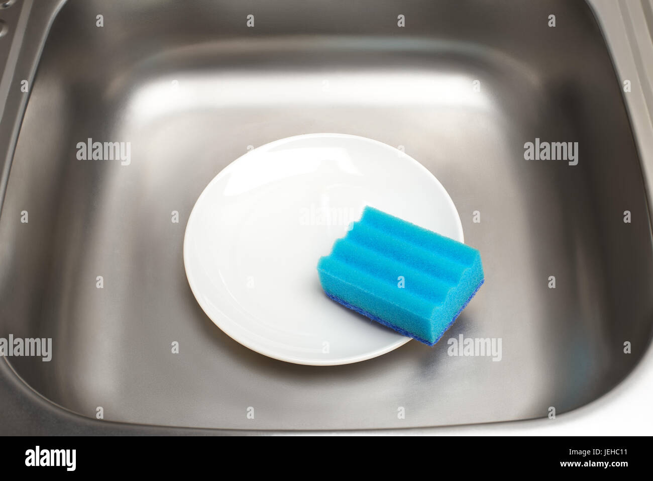 Nahaufnahme der Küchenspüle mit sauberen weißen Teller und blauen Reinigungsschwamm Stockfoto