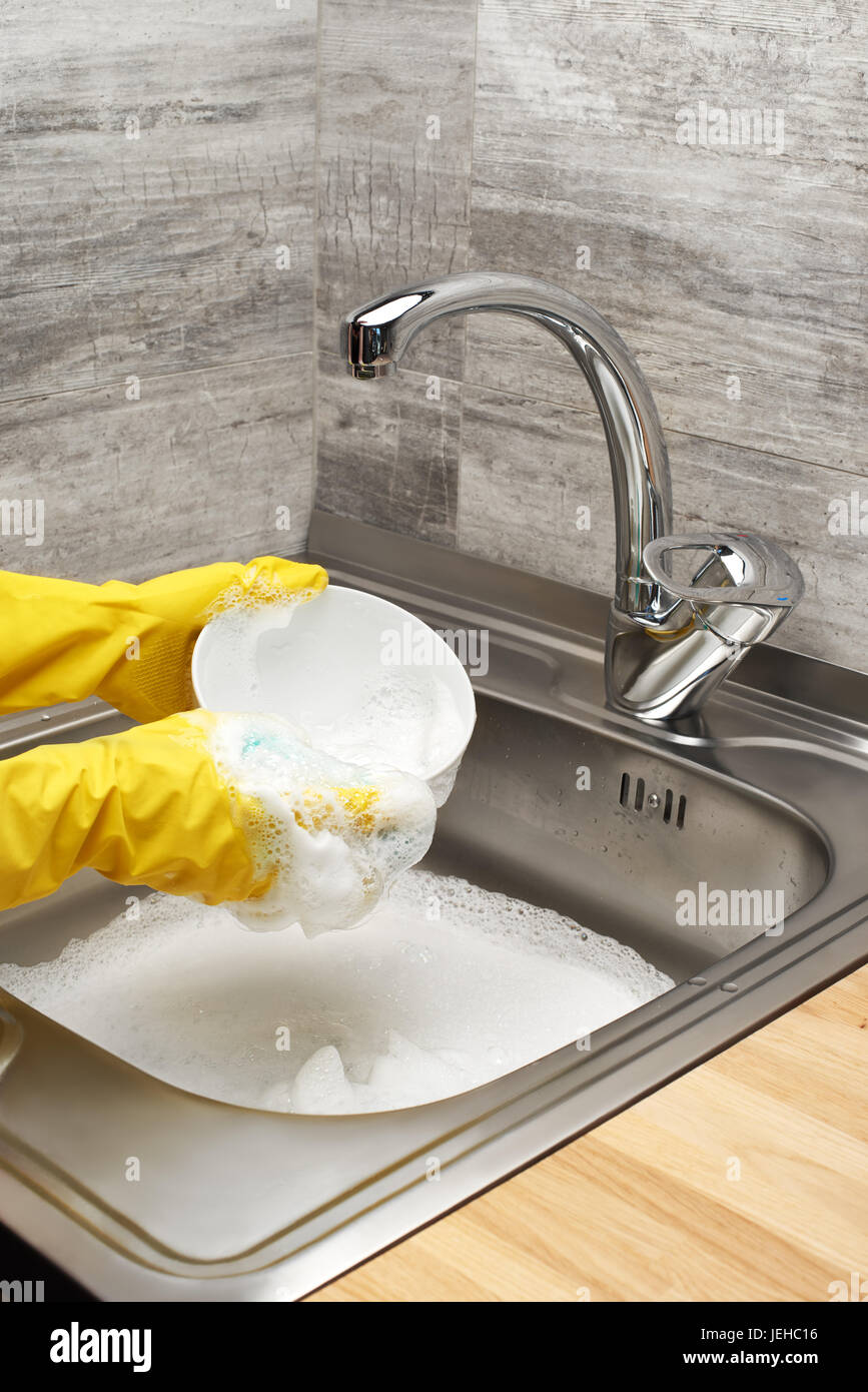 Nahaufnahme von weiblichen Händen Gummischutz Handschuhe waschen Schüssel weiß mit blauen Reinigung gegen Küchenspüle voller Schaum Schwamm gelb Stockfoto