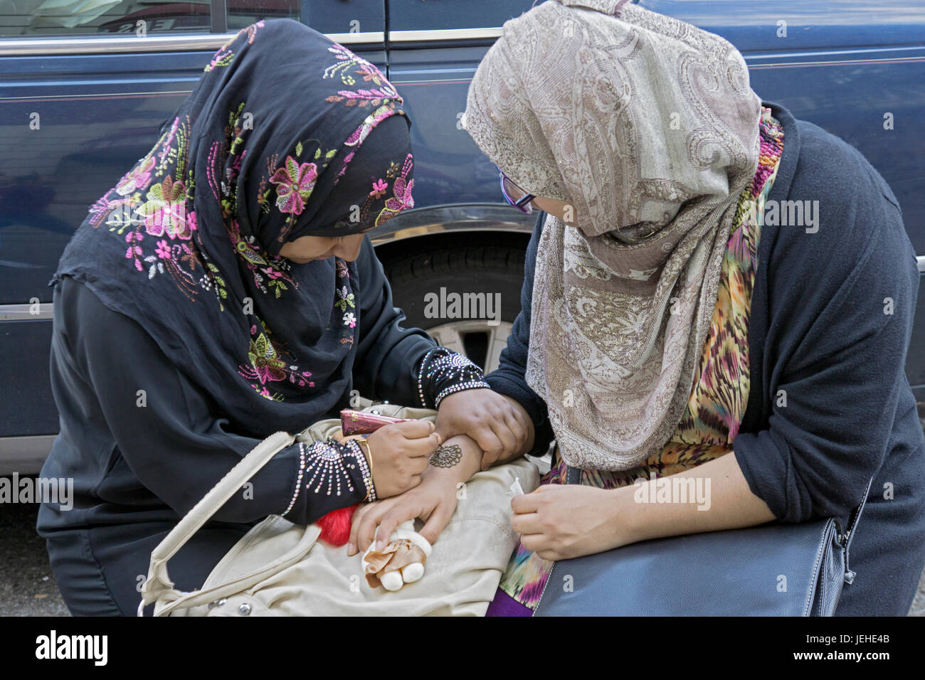 Eine islamische Frau in traditioneller Kleidung schmückt eine Dame Hand mit Henna, Eid Al Fitr Urlaub markiert das Ende auf Ramadan zu feiern. In Queens, New York Stockfoto