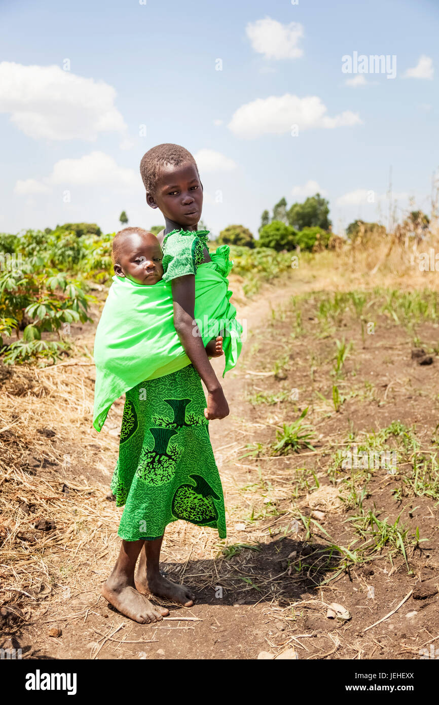 Ein junges Mädchen trägt ein Baby auf dem Rücken in einer Schlinge; Uganda Stockfoto