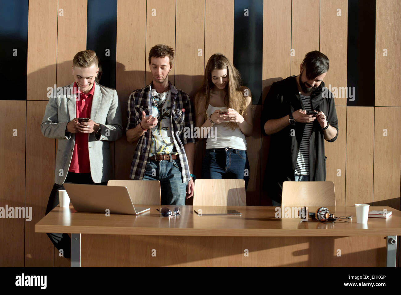 Vier Freunde in der Nähe der Holzwand mit den Telefonen in ihren Händen. Casual-Lifestyle. Stockfoto