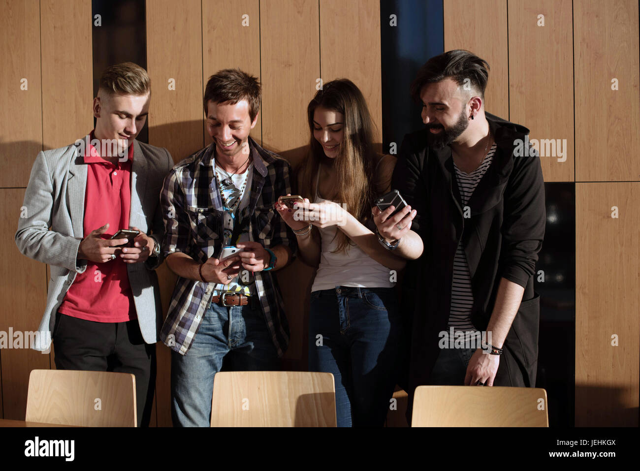 Vier junge und attraktive Menschen, die Spaß mit ihrer Gadgets. Menschen Telefone in ihren Händen halten und sprechen. Stockfoto