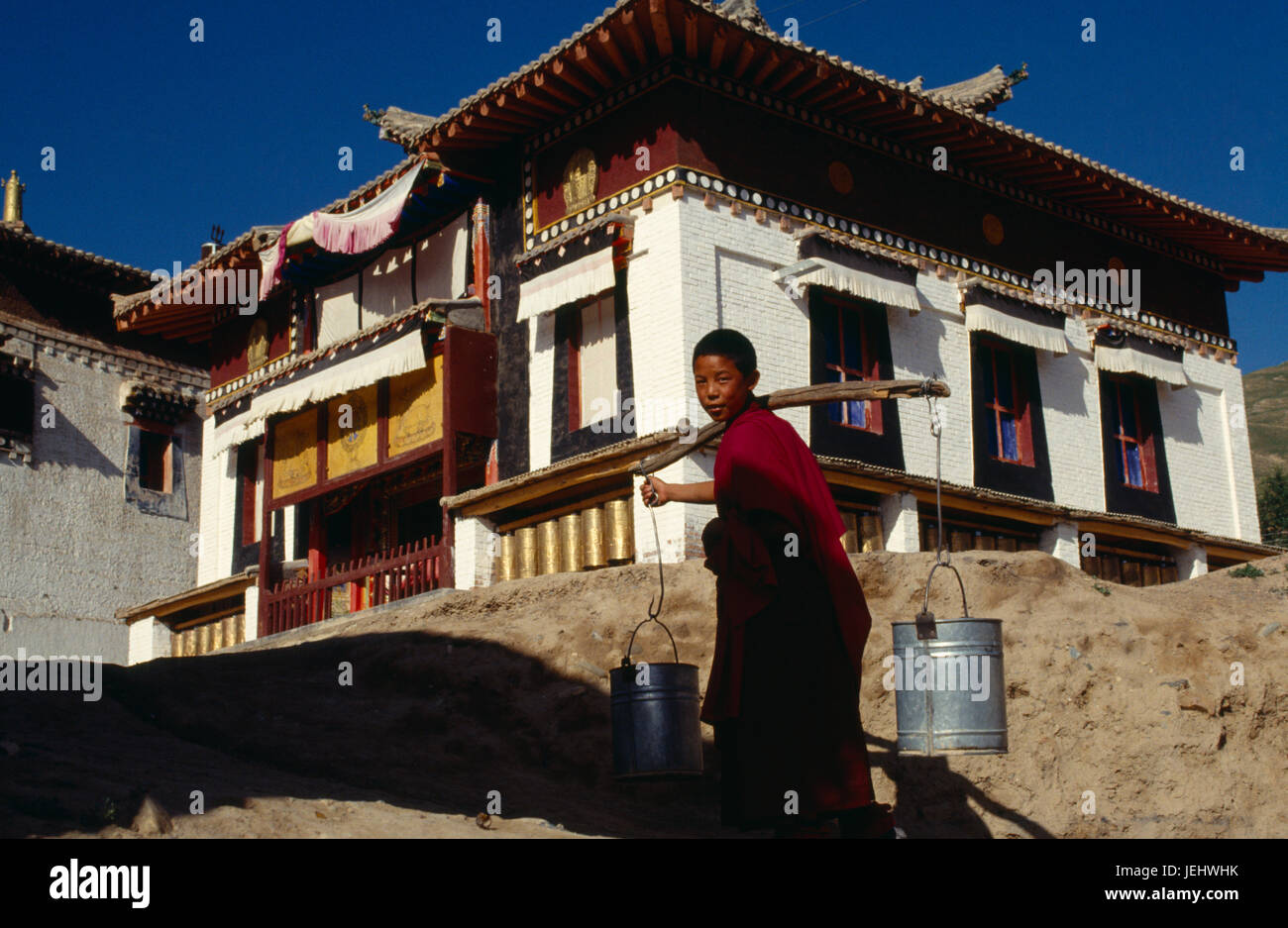 China, Qinghai, General, junger Mönch Wasser bis zu einem Tempel in zwei Eimer auf einem Mast über der Schulter tragen. Stockfoto