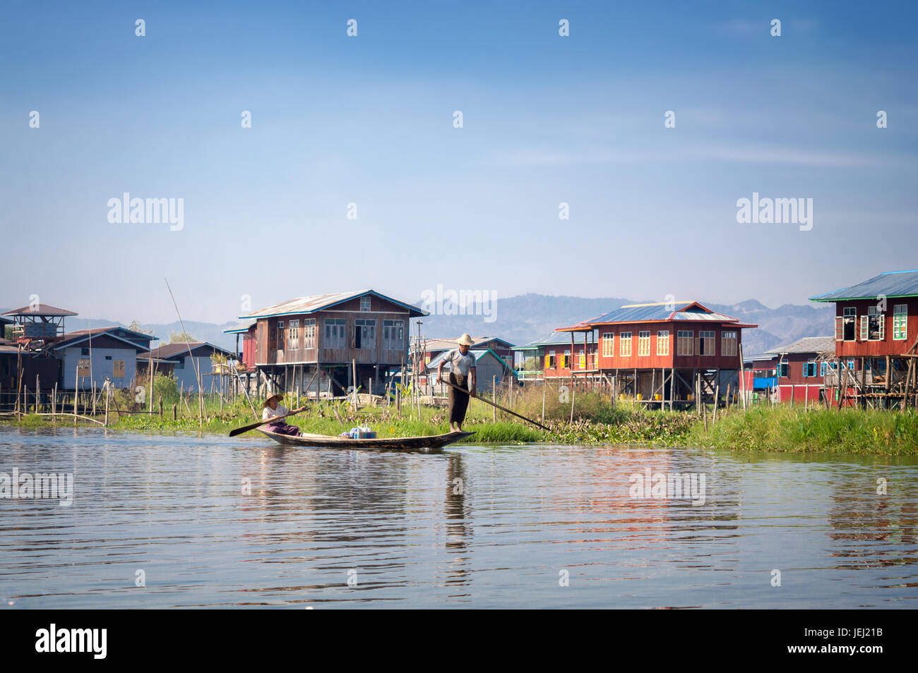 Häuser auf Holzpfählen und Burmesen in einem Boot in einem Dorf am Inle-See, Burma, Myanmar Stockfoto