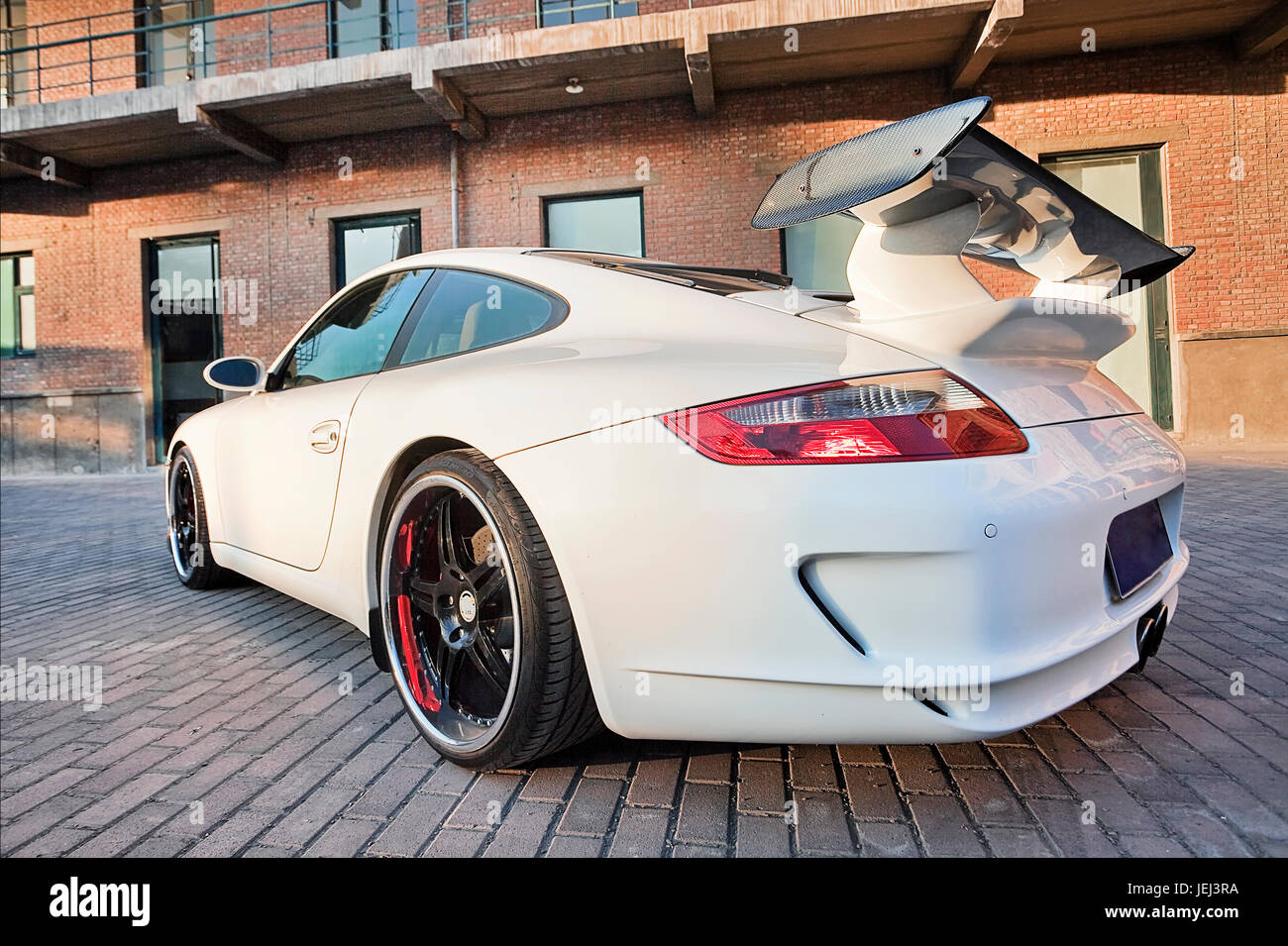 PEKING-NOV. 8. Kundenspezifischer weißer Porsche 911 mit schwarzen Leichtmetallfelgen und massivem Heckspoiler gegen altes Ziegelgebäude. Stockfoto