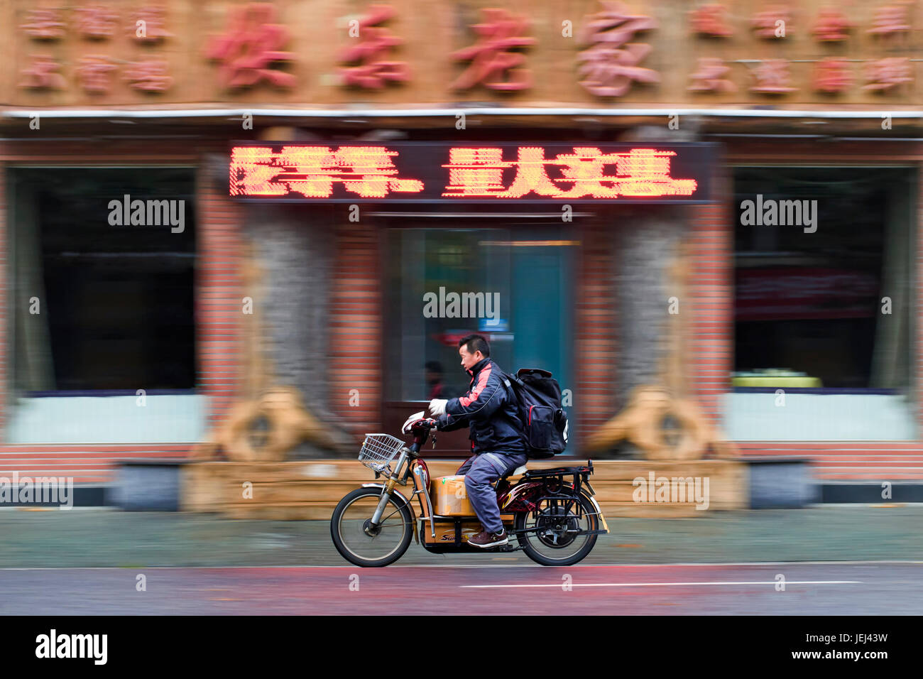 DALIAN-NOV 11, 2012. Mann auf einem Elektrofahrrad. Auf den Straßen chinesischer Städte wimmeln Elektrofahrräder. Etwa 120 Millionen davon sind dort. Stockfoto