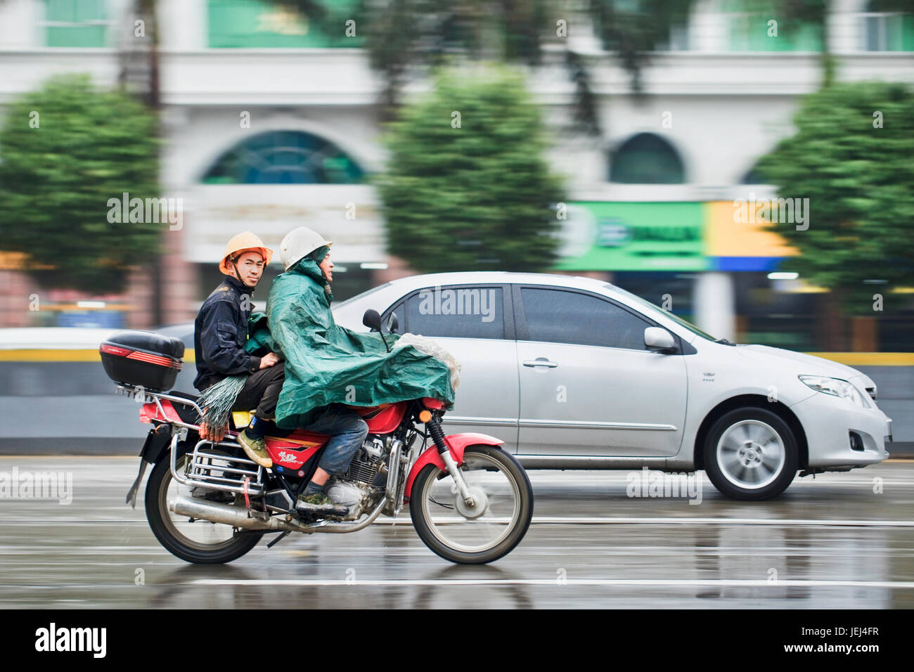 GUANGZHOU-FEB. 25, 2012. Motorrad-Taxi im Regen mit Passagier mit städtischen Szene in Bewegung Unschärfe auf dem Hintergrund. Stockfoto