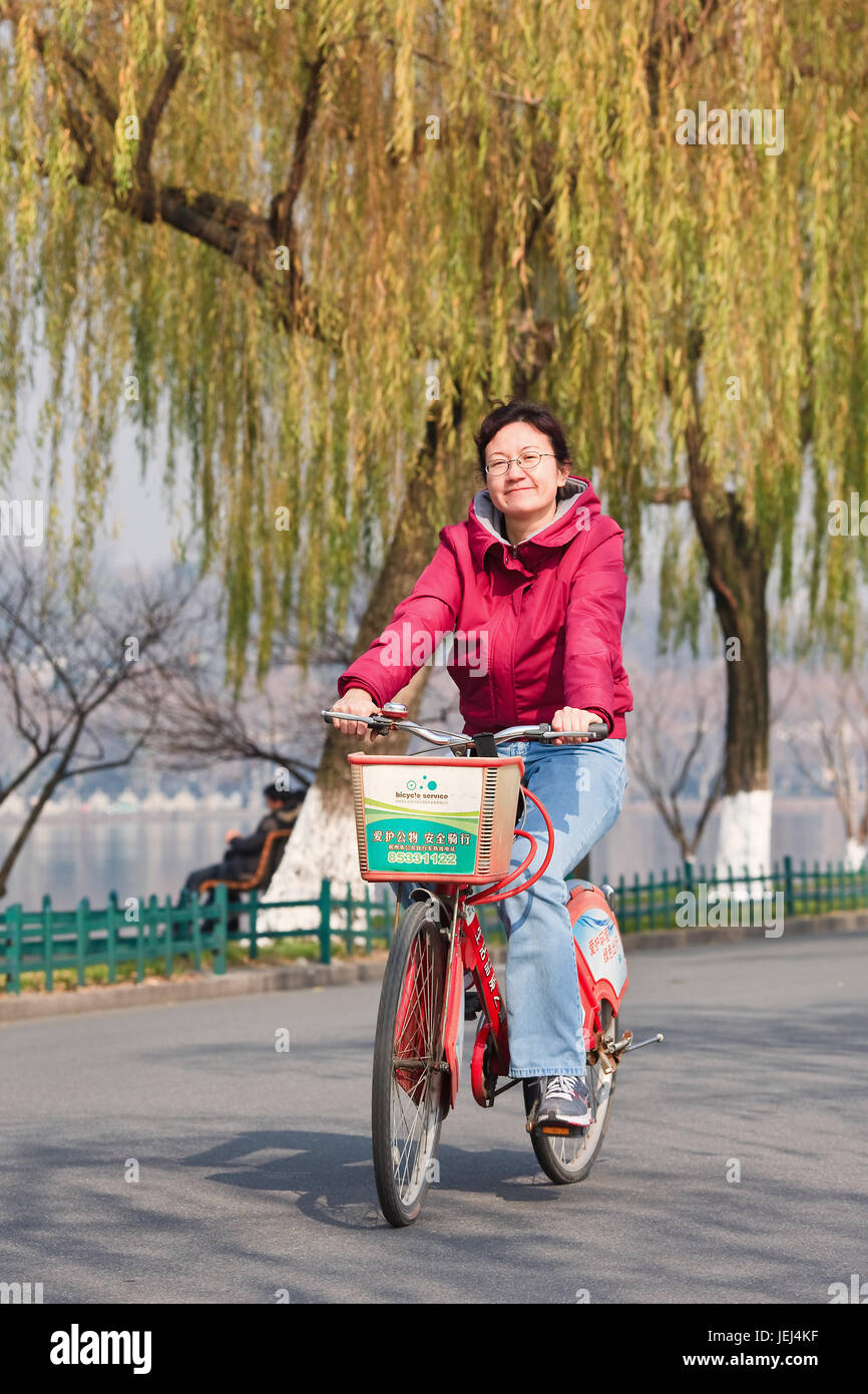 HANGZHOU, 23. DEZEMBER 2009. Fröhliche Frau auf Leihfahrrad. Derzeit betreibt Hangzhou mit 250,000 Fahrten täglich das größte Bikeshare-Programm der Welt. Stockfoto