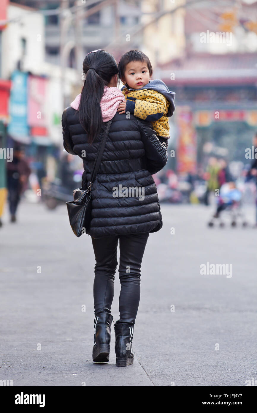 HENGDIAN - 29. DEZEMBER 2014. Junge Frau trägt einen niedlichen Jungen. Die Kommunistische Partei Chinas kündigte 2013 an, die Ein-Kind-Politik zu lockern. Stockfoto