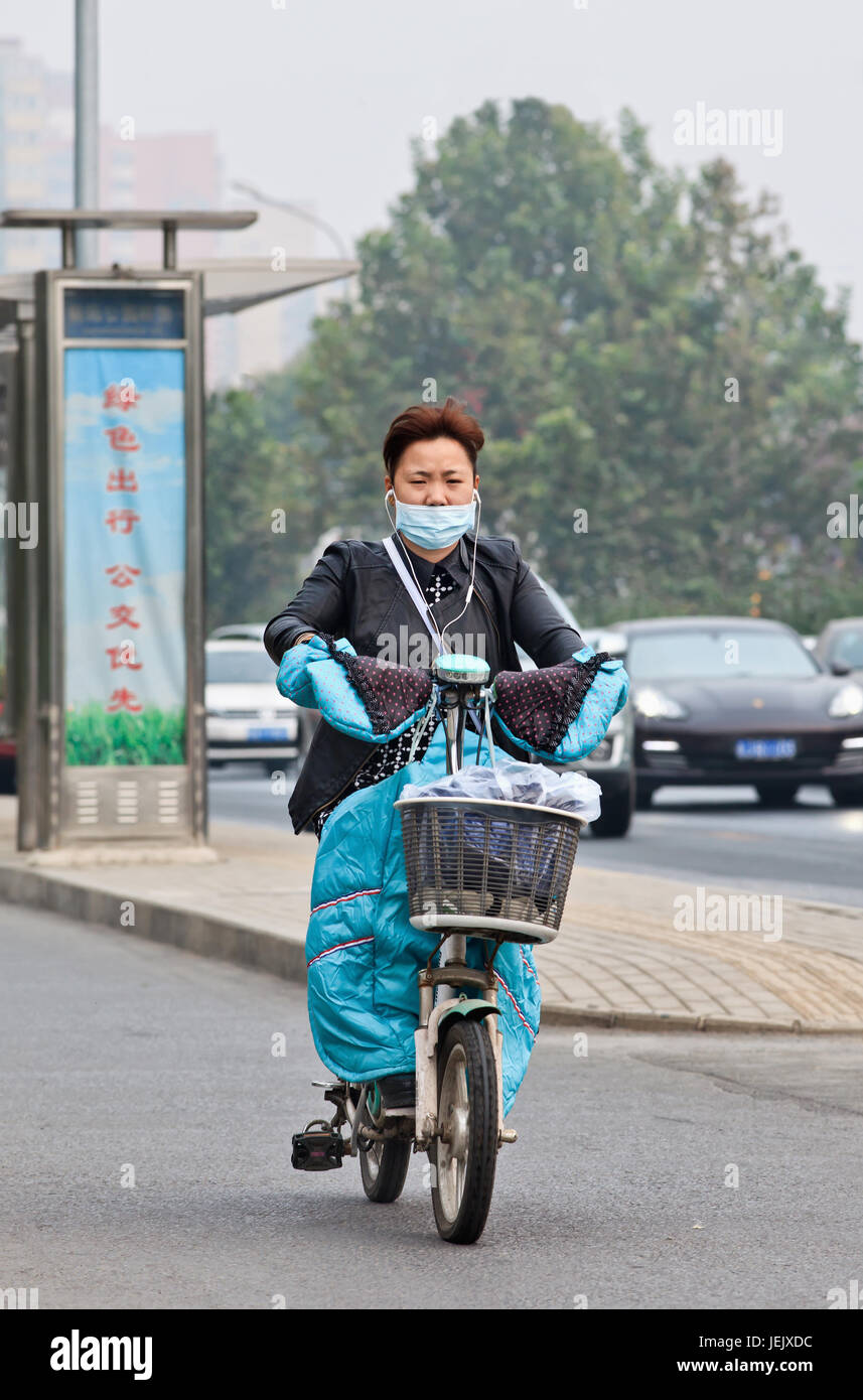 PEKING-OCT. 19, 2014. Frau mit Mütze auf einem E-Bike. Peking erhöhte seinen Smog auf Orange, weil die Luftqualität eine gesundheitliche Bedrohung ist. Stockfoto