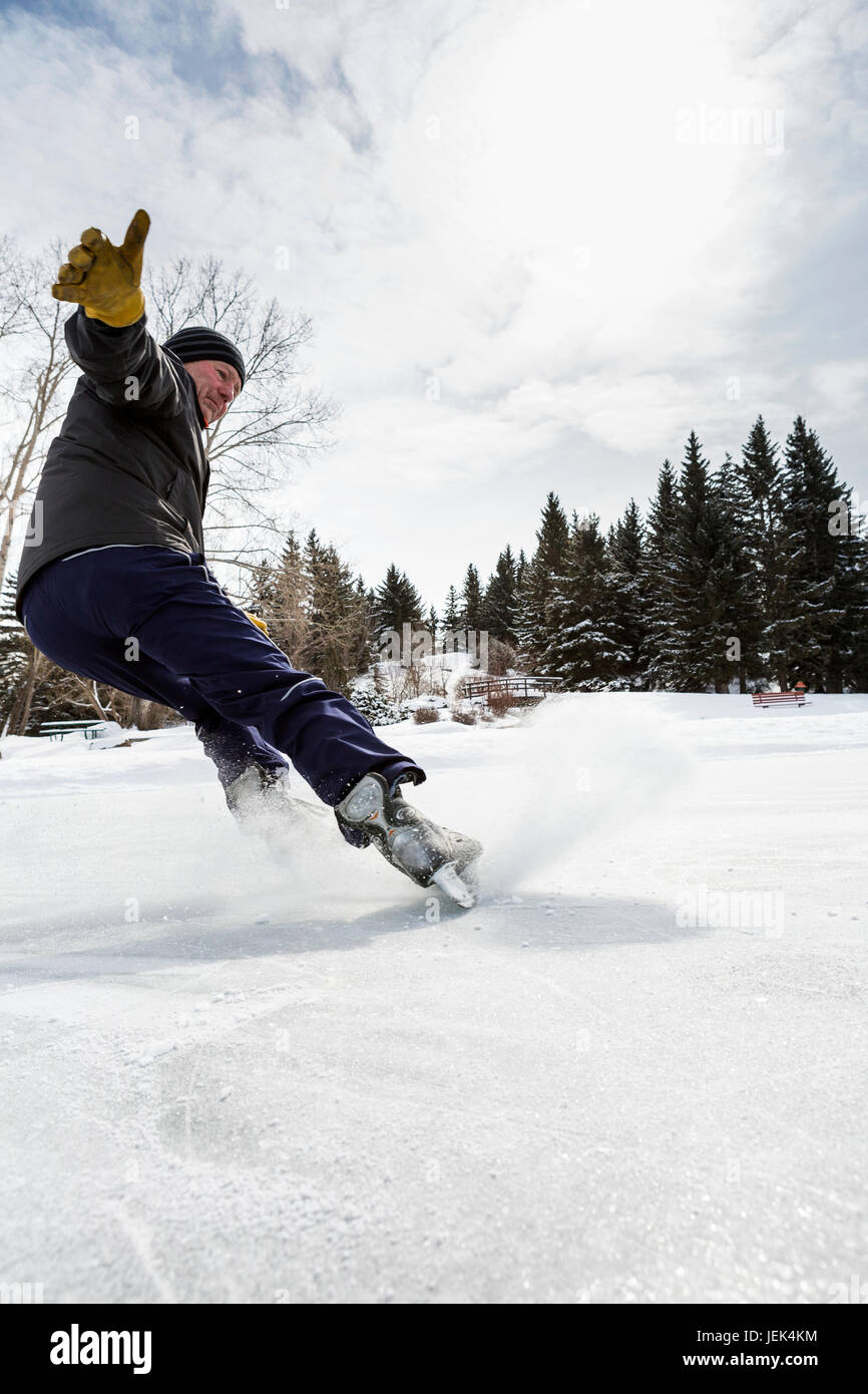 Männlich zu einem Anschlag auf Skates mit Eisspray gleiten; Calgary, Alberta, Kanada Stockfoto