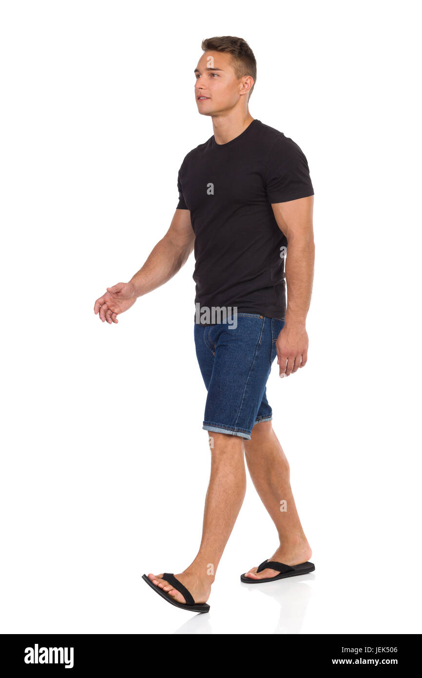 Junger Mann zu Fuß in schwarzes t-Shirt, Jeans-Shorts und schwarzen Sandaletten. Voller Länge Studio gedreht isoliert auf weiss. Stockfoto