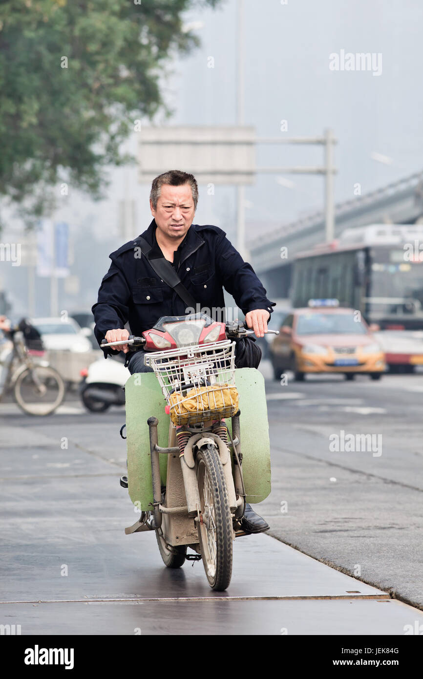 PEKING-OKTOBER 11 ,2014. Mann auf einem elektrischen Fahrrad im Stadtzentrum. Es ist ein sehr verbreitetes Verkehrsmittel in chinesischen Städten. Stockfoto