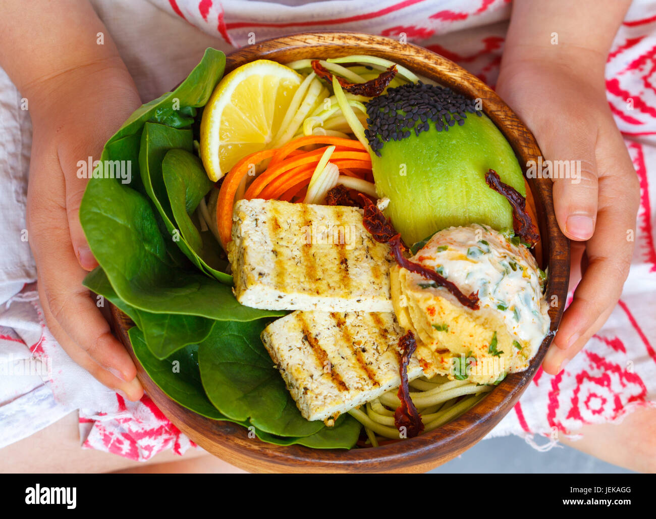 Buddha-Schüssel mit gegrilltem Tofu und Gemüse in die Hände des Kindes. Kind-Vegan-Konzept. Stockfoto