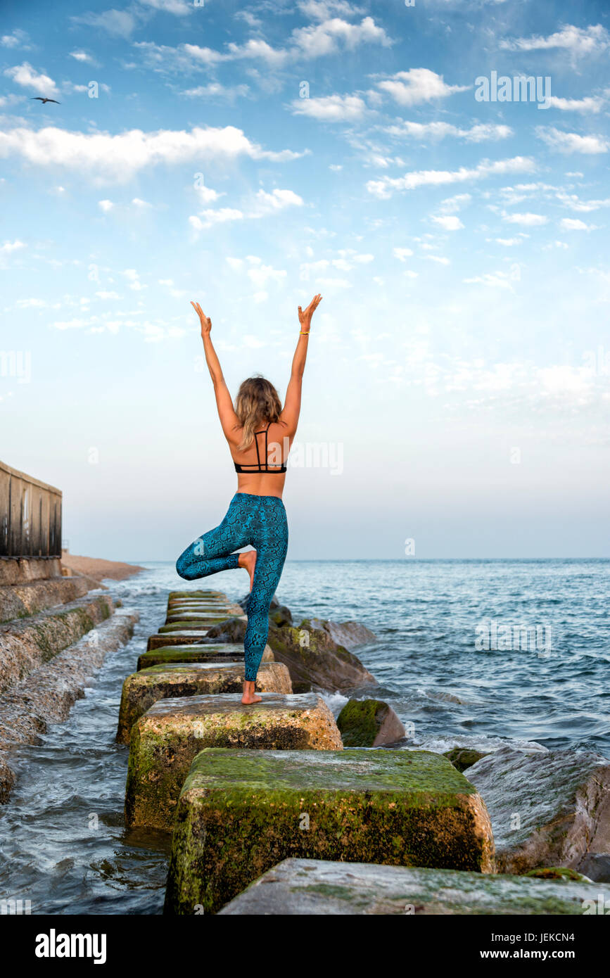 Frau, Yoga zu praktizieren, indem Sie das Meer stehen auf Felsen Stockfoto