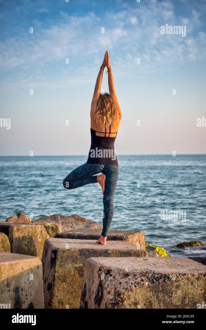 Frau, Yoga zu praktizieren, indem Sie das Meer stehen auf Felsen Stockfoto