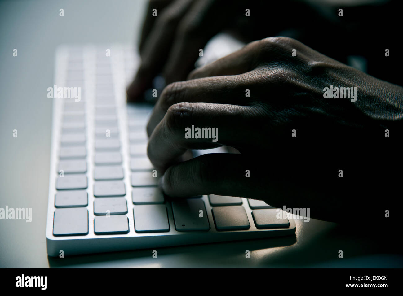 Nahaufnahme eines jungen Mannes, die Eingabe in eine Computer-Tastatur in Finsternis, mit einem dramatischen Effekt Stockfoto