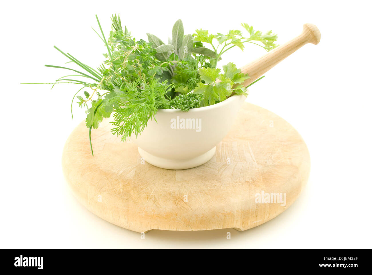 Eine Auswahl von Kräutern in einem Creme Mörser mit Stößel, stehend auf hellem Holz Schneidebrett die Verschleißerscheinungen zeigt.  Isoliert gegen weiße backg Stockfoto