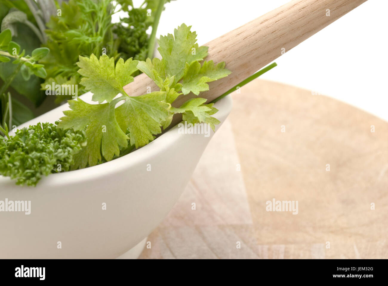 Nahaufnahme von einer Auswahl von Kräutern in einer Creme farbige Mörser mit Stößel auf abgenutzte Schneidbrett aus Holz.  Thema schneidet am linken Rand des Rahmens.  Isolat Stockfoto