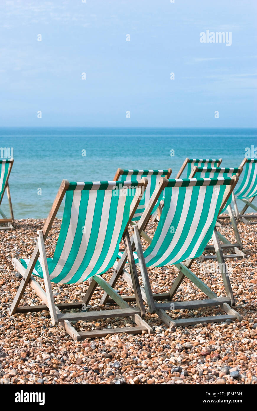 Sieben leere Aqua grüne-weiße gestreifte Liegestühlen mit Blick aufs Meer auf einem Kiesstrand.  Heller, sonniger Tag mit Ble Sky. Stockfoto