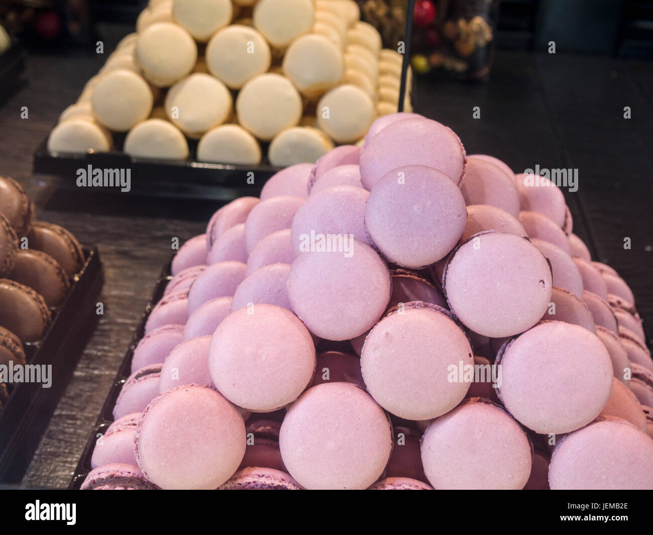 Ein Haufen von rosa Macaron in einem Schaufenster: eine Pyramide geformt Haufen von rosa Längezeichen in einem Schaufenster umgeben von cremig weißer und brauner Schokolade Sorten. Stockfoto