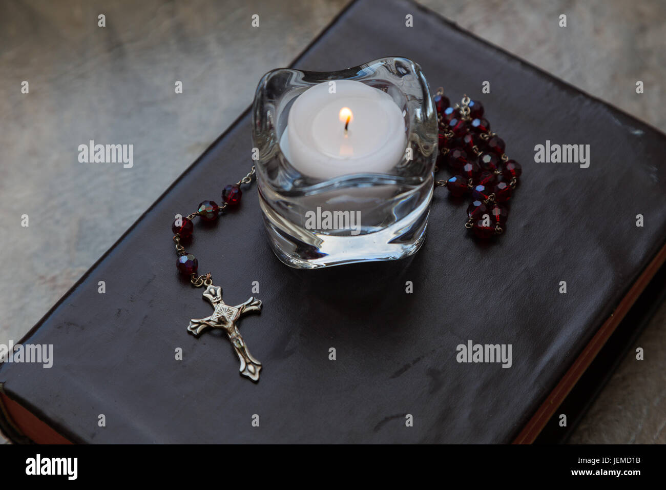 Nahaufnahme einer verwitterten Leder bezogen-Bibel mit einer Reihe von roten Rosenkranz und ein Teelicht Kerze in einem Glas Kerzenständer. Stockfoto