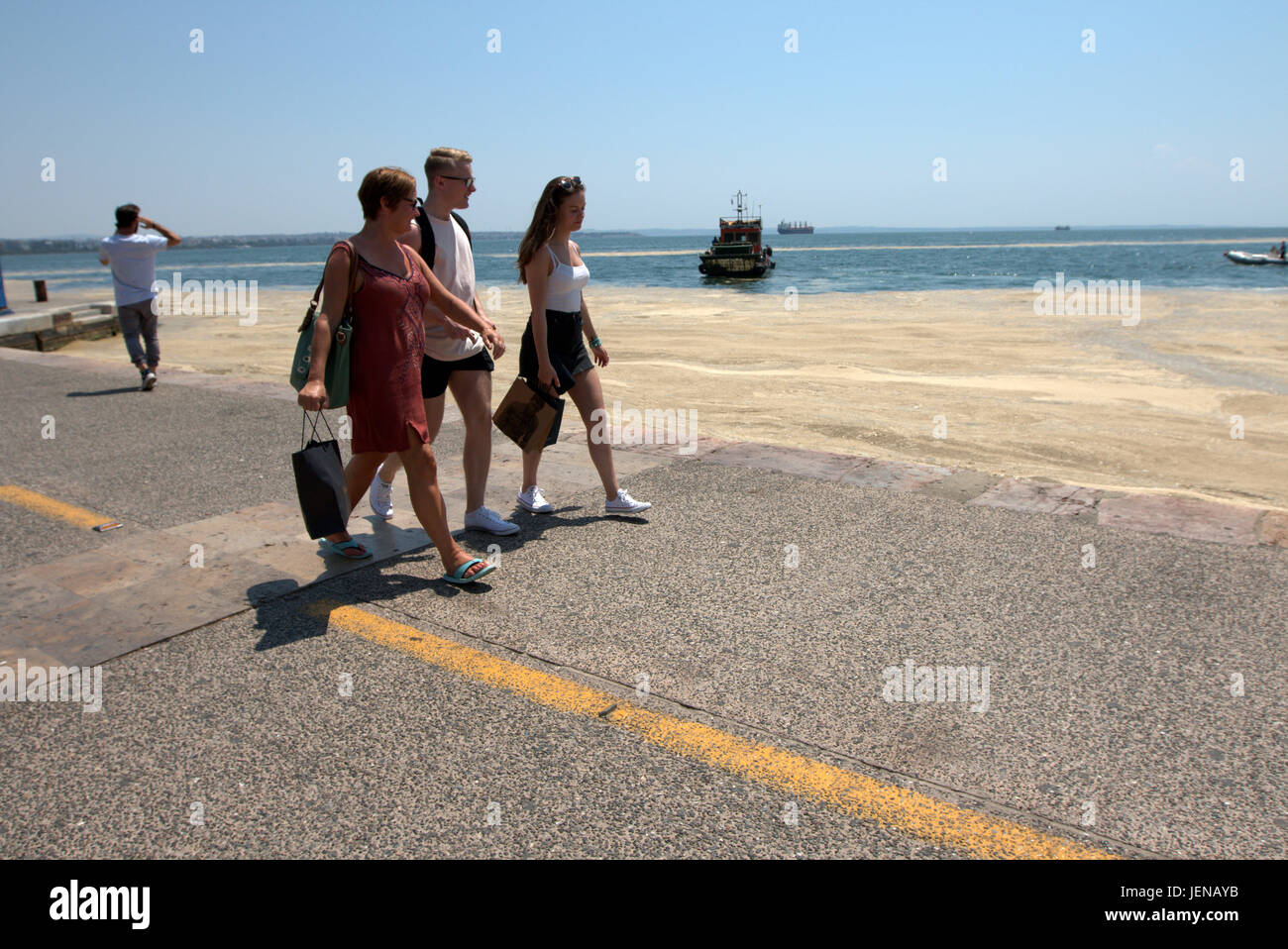 Thessaloniki, Griechenland. 27. Juni 2017. Touristen zu Fuß vorbei an eine rote Flut Phänomen betroffen Küste der nördlichen Hafen der griechischen Stadt Thessaloniki. Red Tide ist eine gebräuchliche Bezeichnung für ein Phänomen bekannt als eine Algenblüte, verursacht durch Arten der Dinoflagellaten, die auf eine rote oder braune Farbe. Kredit Kredit: Orhan Zolak/Alamy Live-Nachrichten Stockfoto