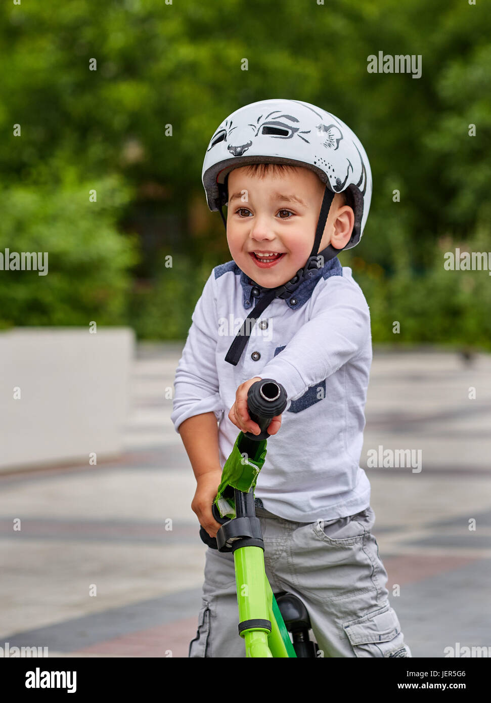 Kind Junge im weißen Helm auf seinem ersten Fahrrad mit Helm fahren. Fahrrad ohne Pedale. Stockfoto