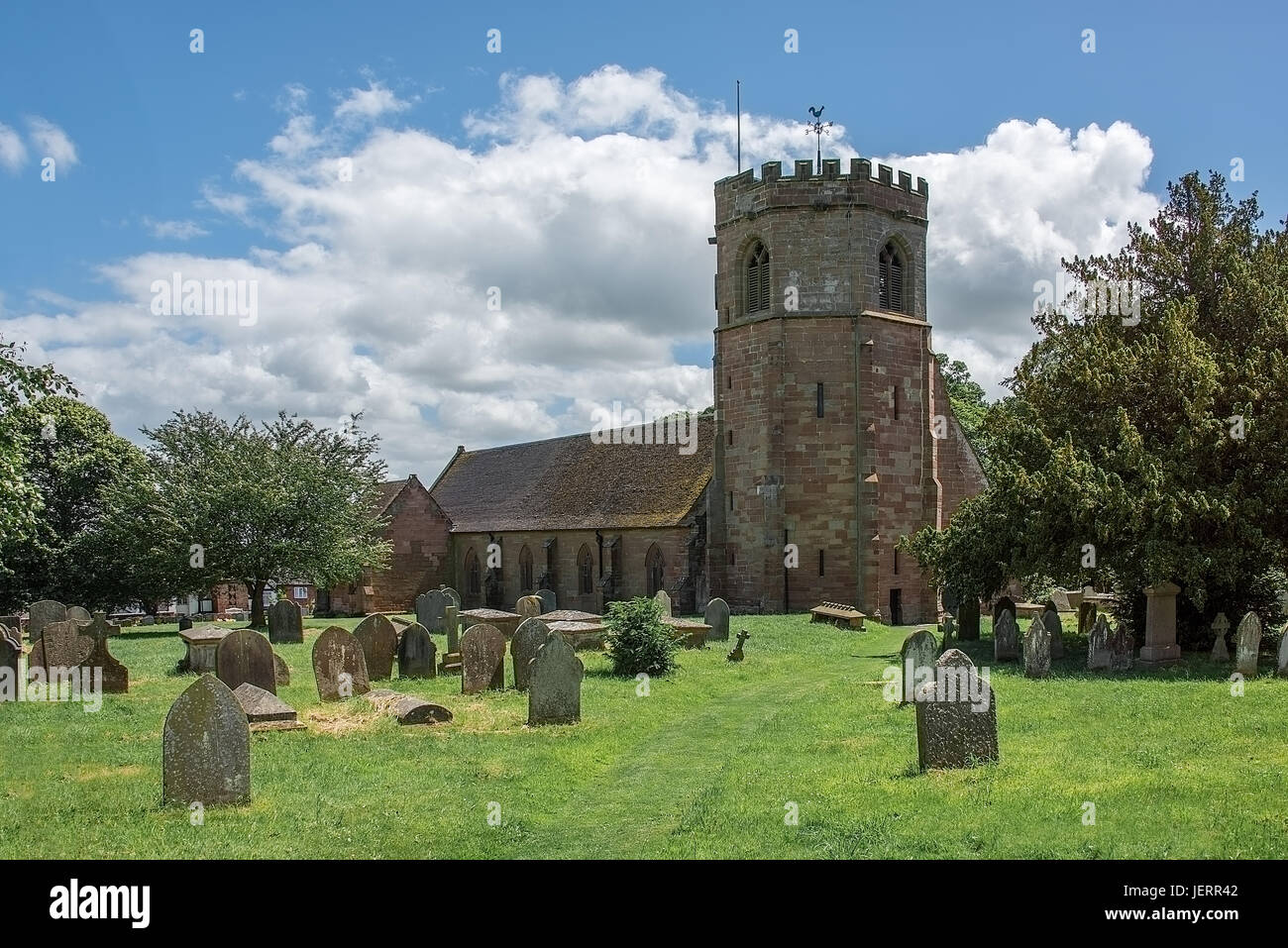 Ein horizontales Bild eines typischen englischen Country-Dorfes genommen an einem sonnigen Tag mit blauem Himmel und Kirche steht auf einem Friedhof Stockfoto