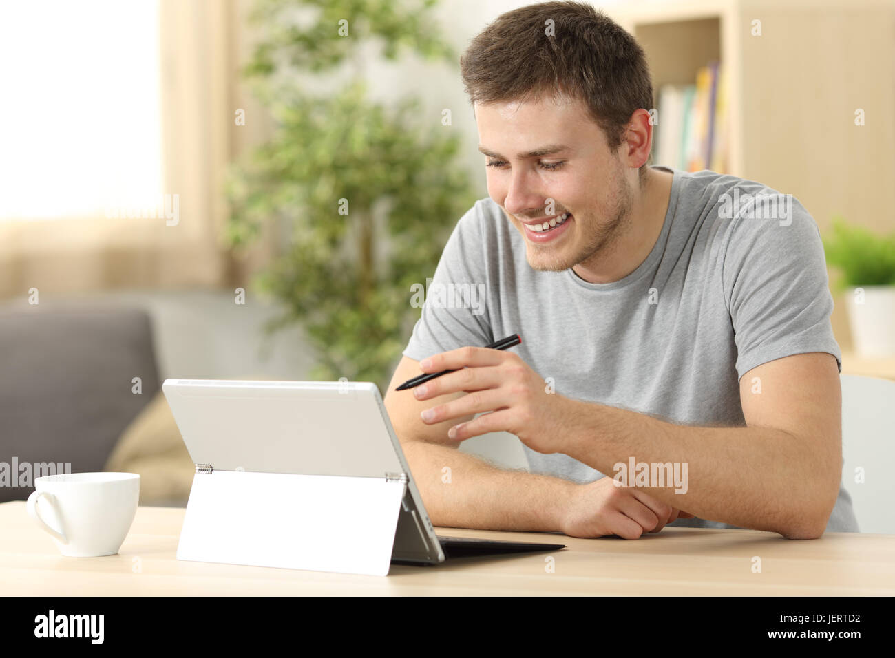 Legerer Mann Suche auf Linie mit einem Tablet mit einem Stift sitzt in einem Schreibtisch zu Hause mit einem Fenster im Hintergrund Stockfoto