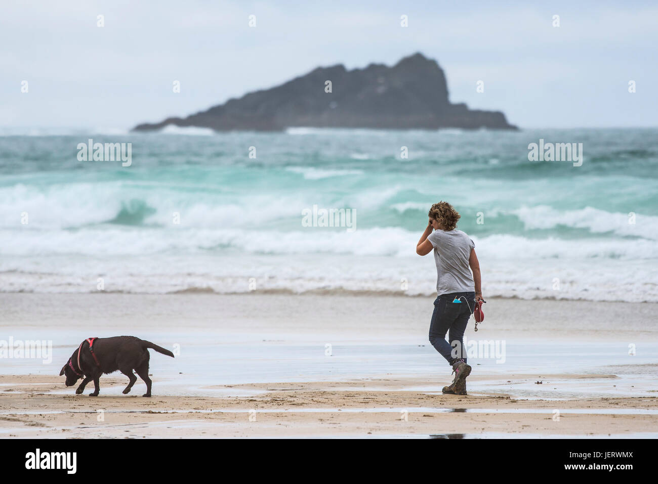 Eine Frau, die ihrem Hund Hund freundlich Fistral Strand in Newquay, Cornwall entlang spazieren. Stockfoto