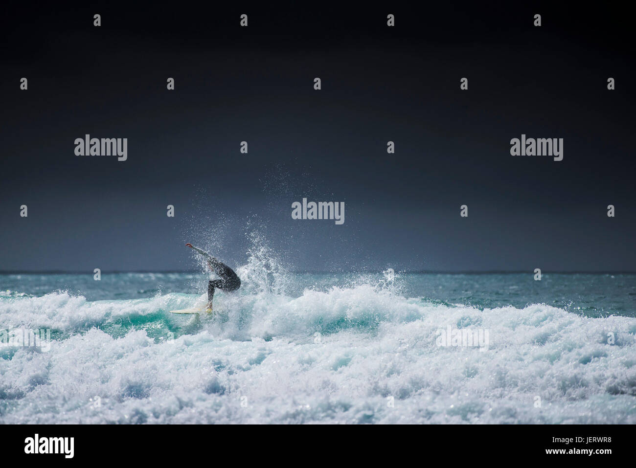 Surfen-UK.  Ein einsamer Surfer eine Welle zu reiten, wie dunkle über der Küste von North Cornwall Wolken. Stockfoto