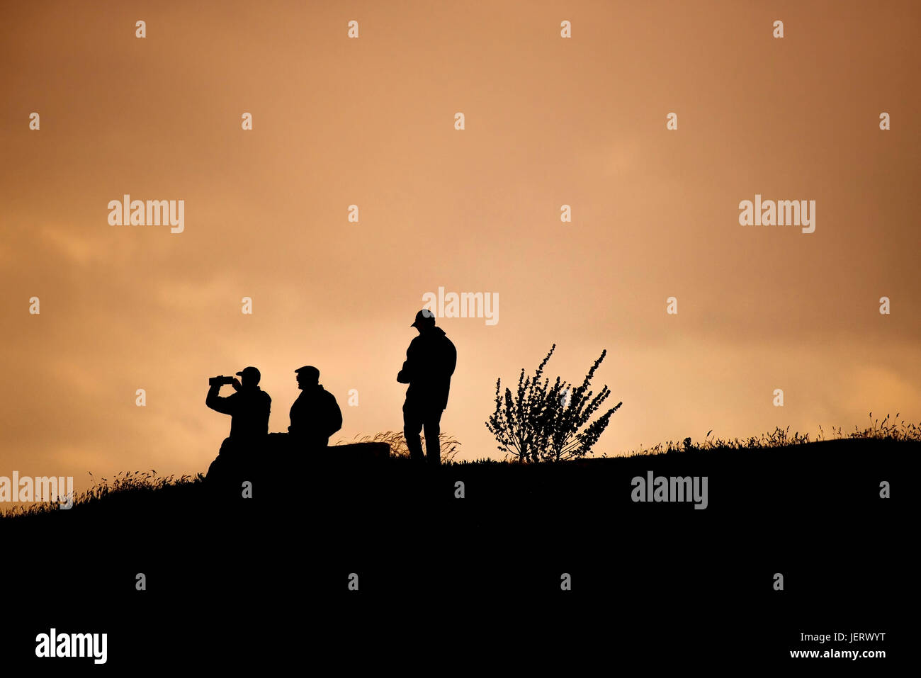 Wie die Sonne über sind Fistral Norden drei Menschen in der Silhouette gesehen. Newquay, Cornwall. Stockfoto