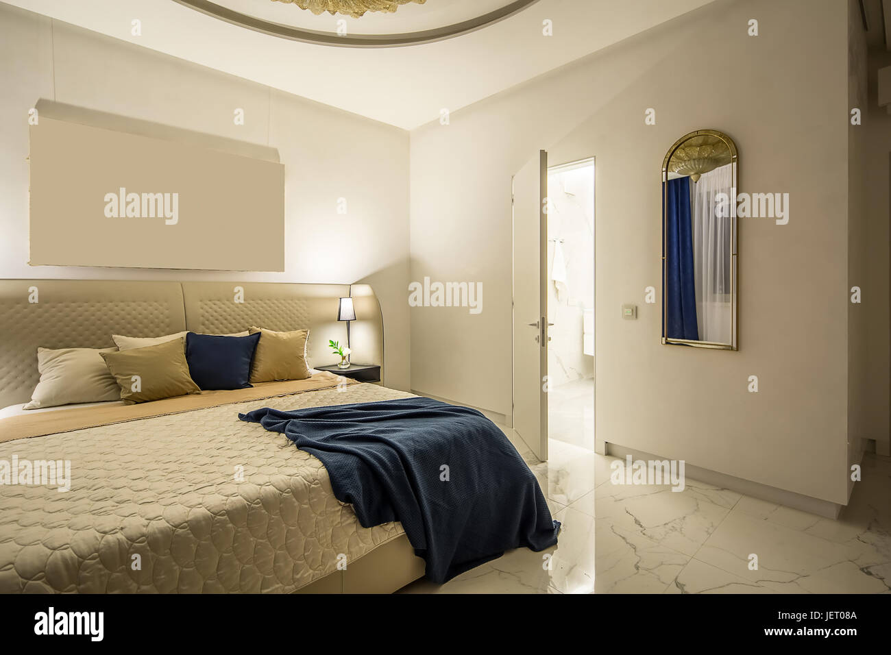 Moderne Schlafzimmer mit weißen Wänden und Licht gefliesten Boden. Gibt es eine Beige Bett mit bunten Kissen und ein blau kariert, Regal mit Blumen in einer Vase, l Stockfoto