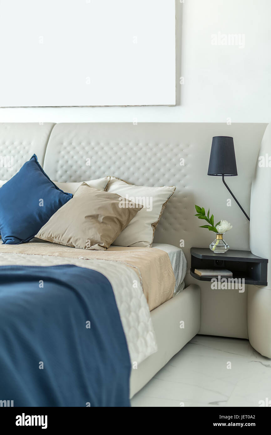 Leichte Bett mit bunten Kissen und Badetücher auf die weiße Wand Hintergrund. Auf der rechten Seite ist ein schwarze Regal mit einer Blume in einer Glasvase und Stockfoto