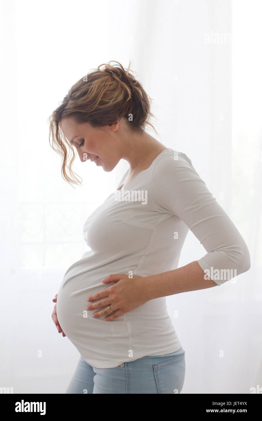 Junge schwangere Frau mit geschlossenen Augen ihren Magen umarmen Stockfoto