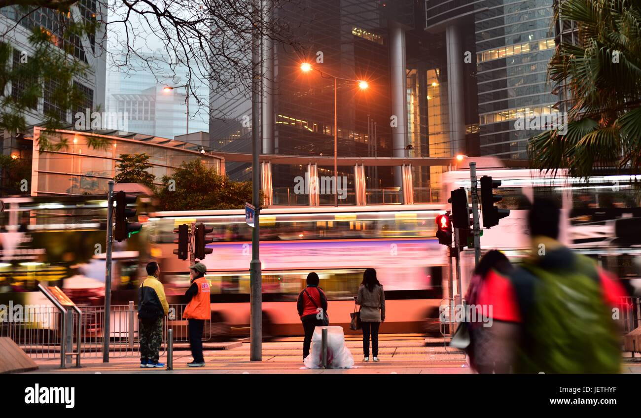 Hong Kong Straßen in den frühen Morgenstunden, mit Bussen auf der Straße, moderne Gebäude im Hintergrund und Menschen auf ihrem täglichen Weg zur Arbeit Stockfoto