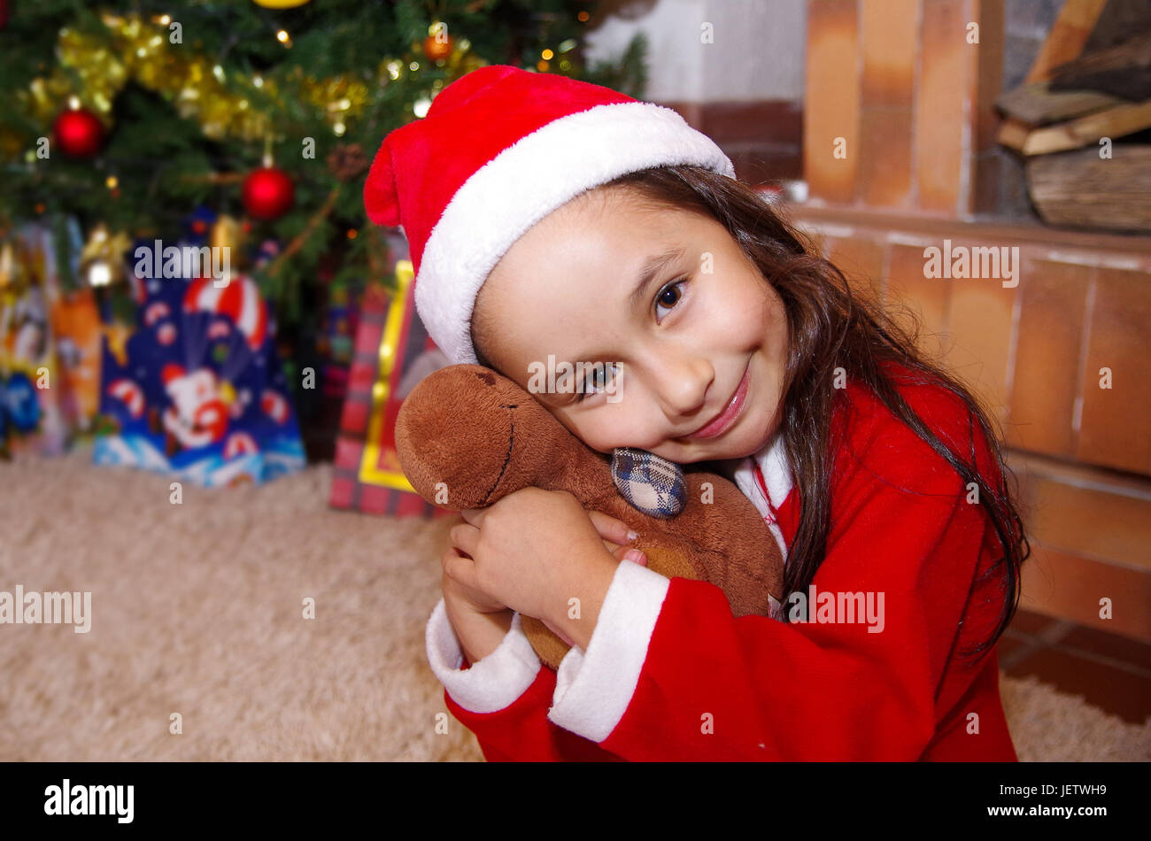 Schönes Lächeln auf den Lippen Litle Mädchen Kleidung ein Weihnachten, umarmt einen Elch Teddy mit einem Weihnachtsbaum-Hintergrund mit einigen Geschenken. Stockfoto