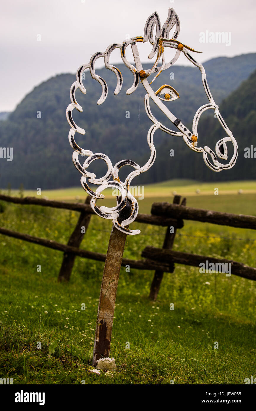 Melden Sie sich bei einem Pferdegesicht auf Rasen mit Bergwald im Hintergrund stehen. Stockfoto