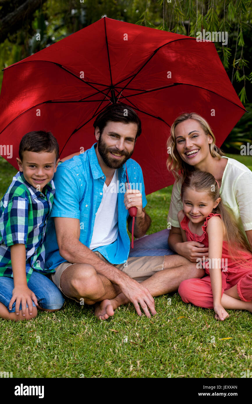 Lächelnd Familie sitzt mit Regenschirm im Hof Stockfoto