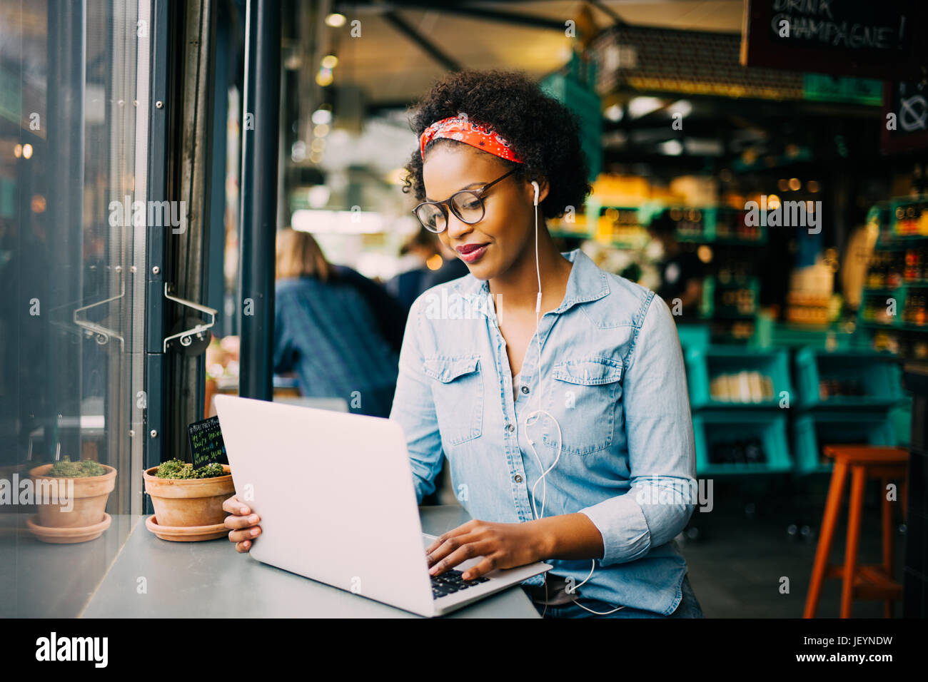 Junge afrikanische Frau saß allein an einem Schalter in einem Café auf einem Laptop arbeiten und Musik über Kopfhörer hören konzentriert Stockfoto