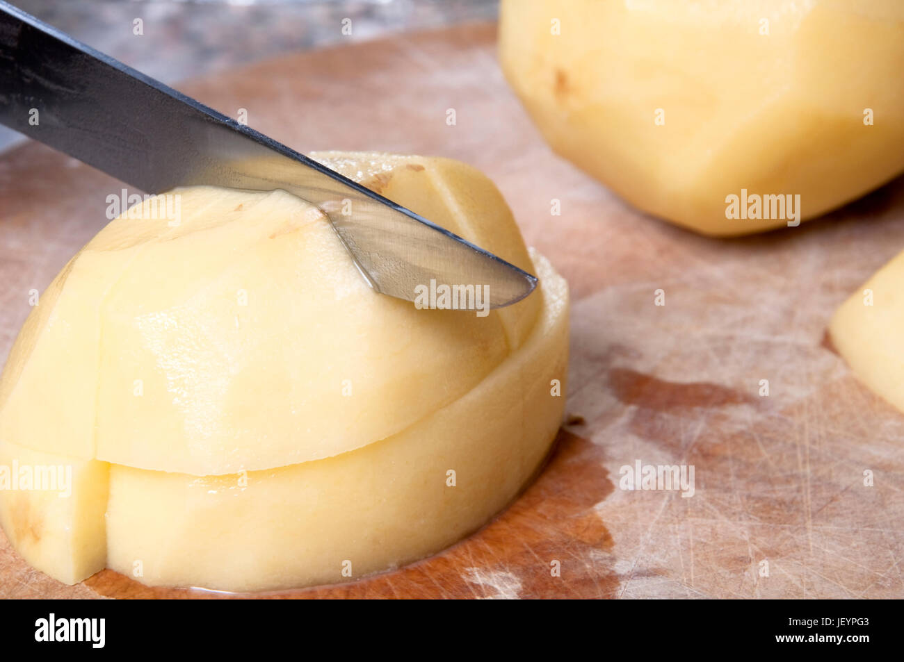 Lauffeuer der Kartoffeln wird gehackt auf einem alten hölzernen Schneidebrett mit sichtbaren Schnittmarken hautnah.  Zähler nach oben im Hintergrund sichtbar. Stockfoto