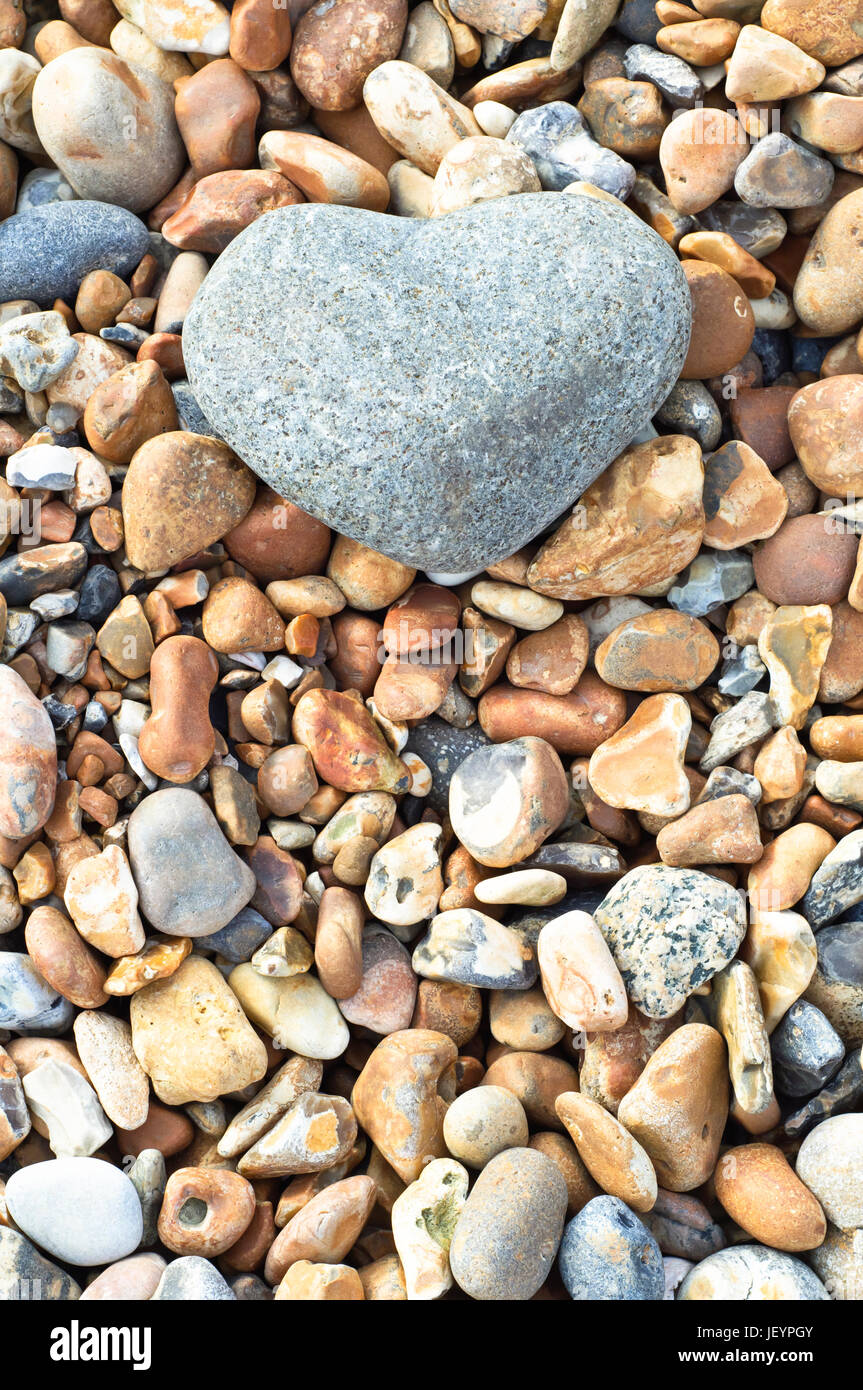 Eine graue herzförmige Stein im oberen Rahmen ruht auf einer Vielzahl von kleineren Steinen.  Im Hochformat (vertikal). Stockfoto