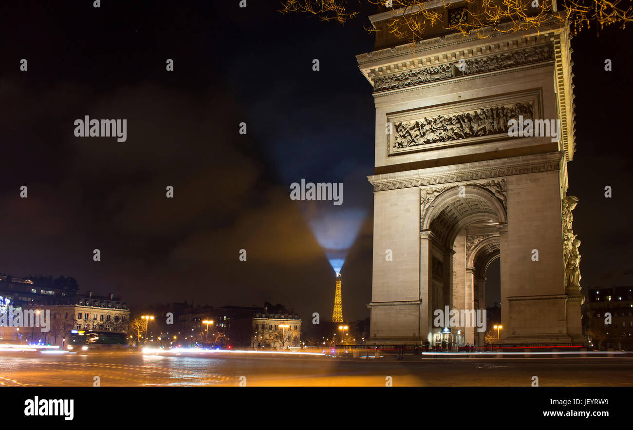 Blick auf den Arc de Triomphe in der Nacht. Eiffel-Turm leuchtet der Himmel in blau im Hintergrund. Lichtspuren von Autos in Bewegung sind auch in der Ansicht. Stockfoto